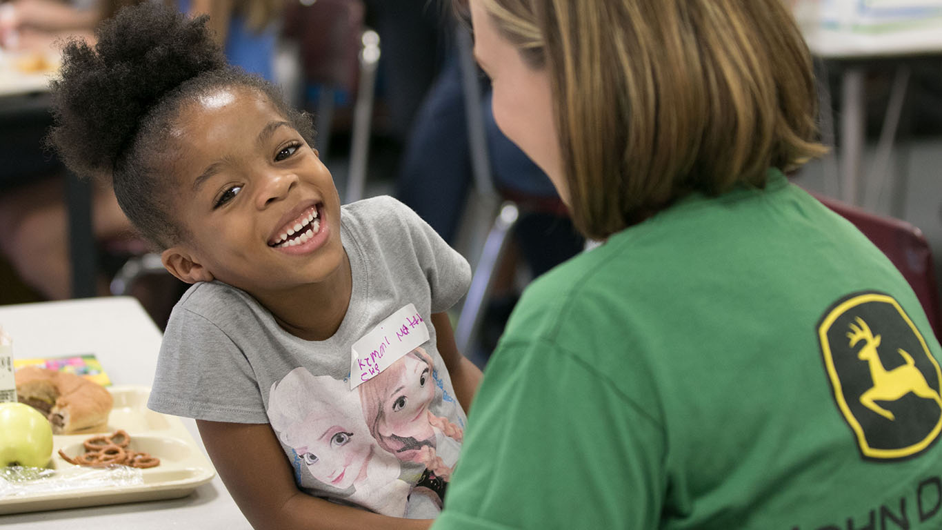 A young girl enjoys lunch with a John Deere employee